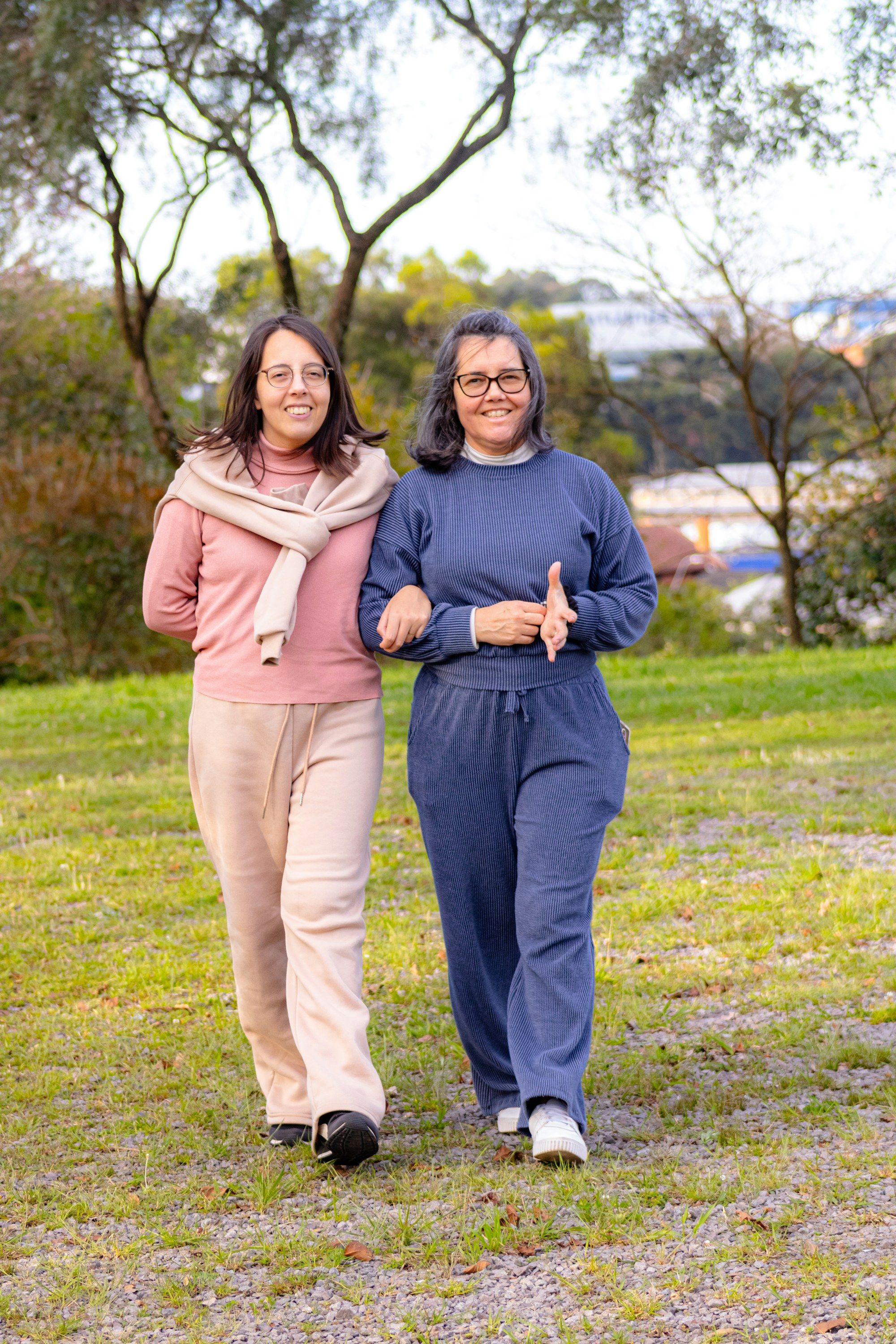 Zwei Frauen gehen untergehakt und lachend durch einen Park